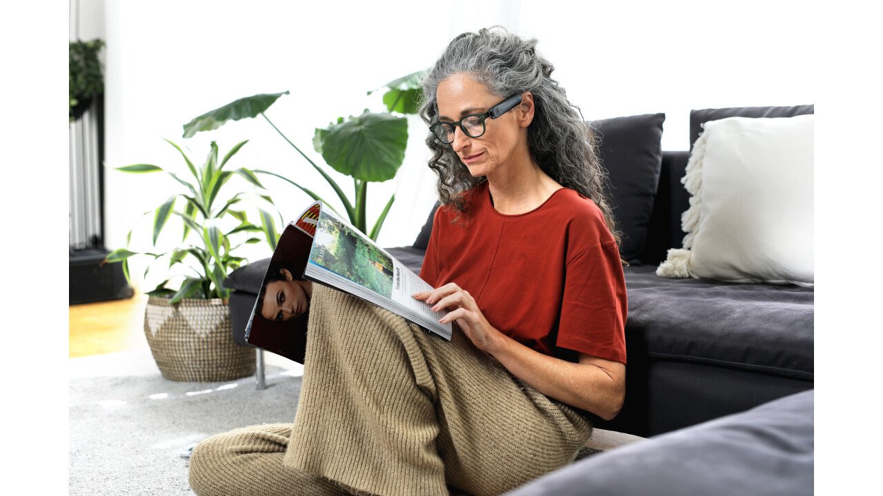 Eine blinde Frau liest eine Zeitschrift. Die OrCam liest ihr den Text vor.